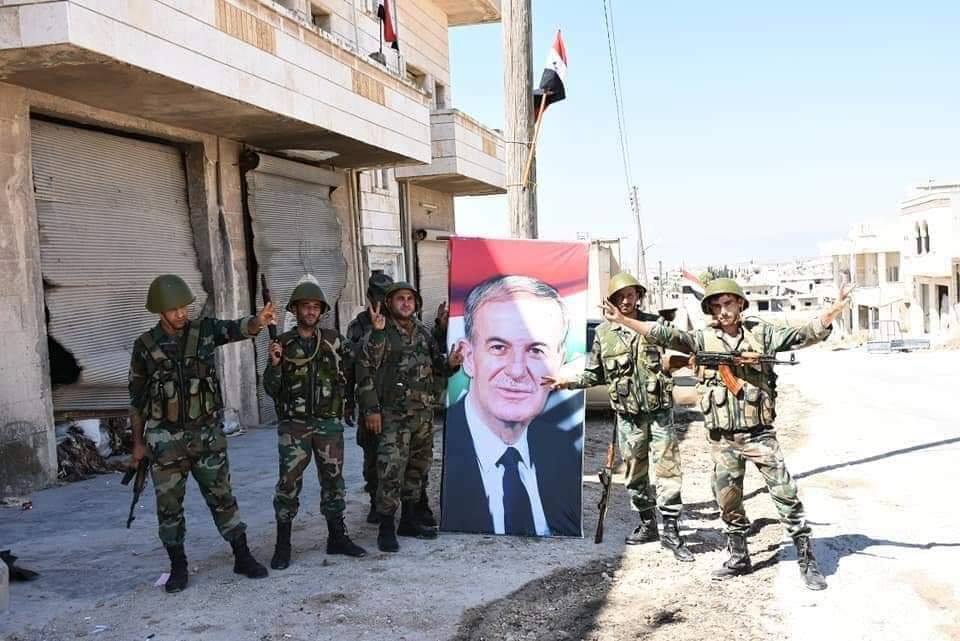Les soldats de l'Armée Arabe Syrienne élèvent le drapeau Syrien et le portrait du défunt Président Hafez Al Assad à Khan sheikhoun.